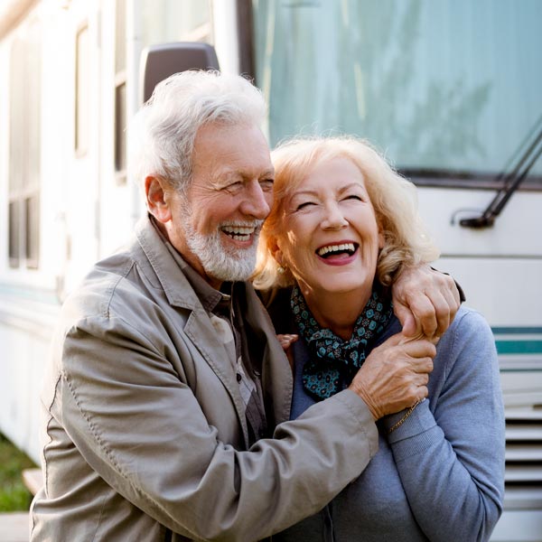 An older couple joyfully laughing after dental implant in front of their RV in Phoenix, AZ